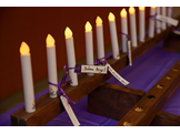 A row of candles with nametags tied to them in purple ribbons.